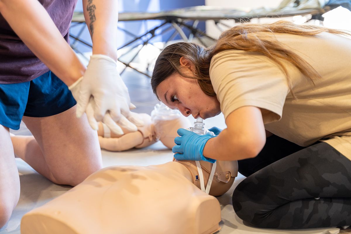 First-aid trainees practice CPR on a mannequin as a kneeling woman performs chest compressions in a focused training session.